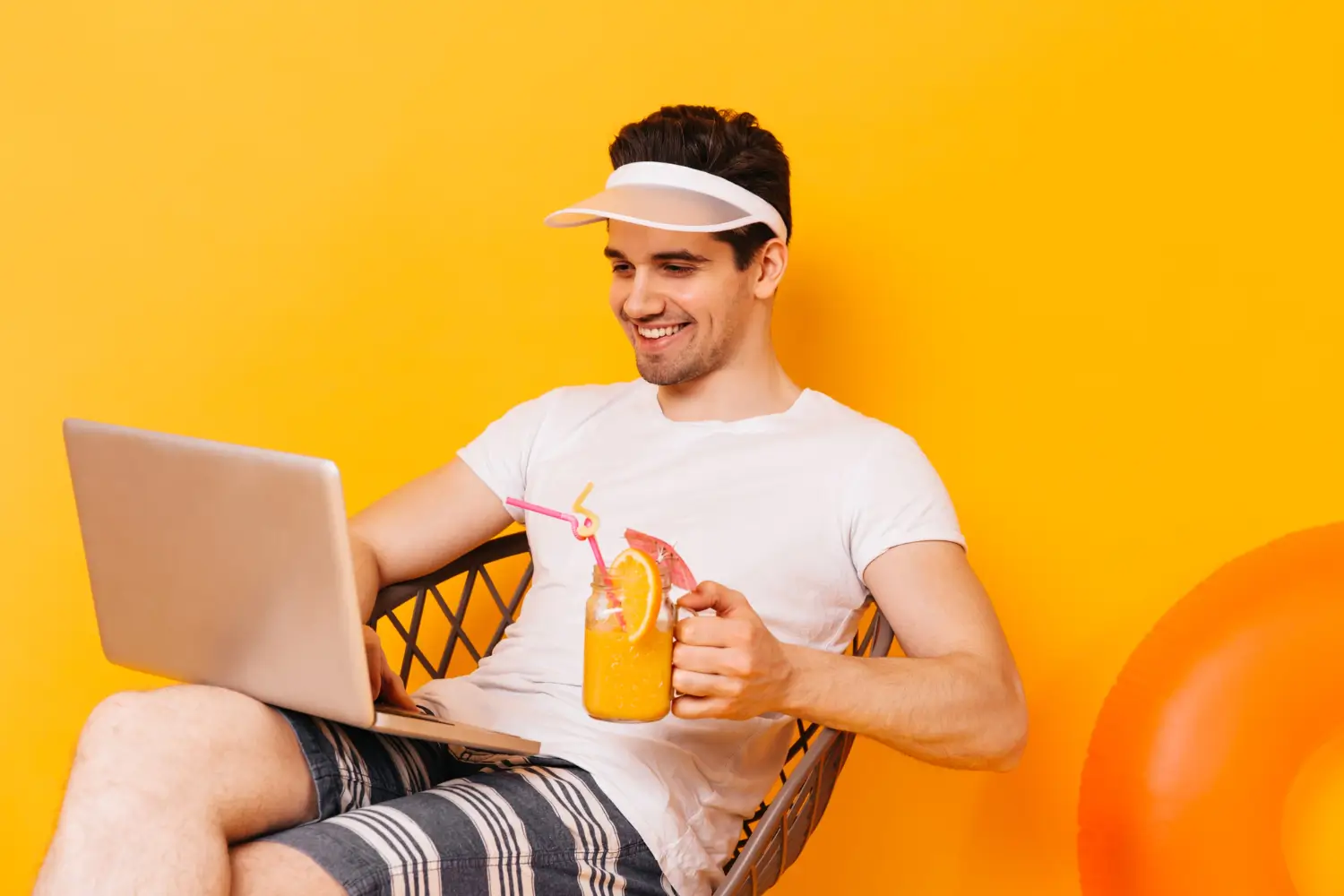 Smiling man using a laptop while holding a glass of orange juice.