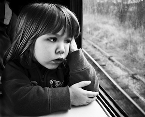 A bored child staring out of a train window.