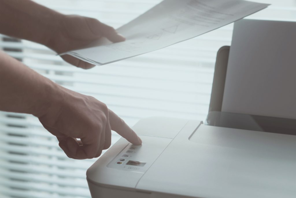 A person using a printer while holding a piece of paper.