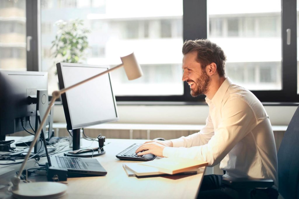 A smiling man sitting at a computer.