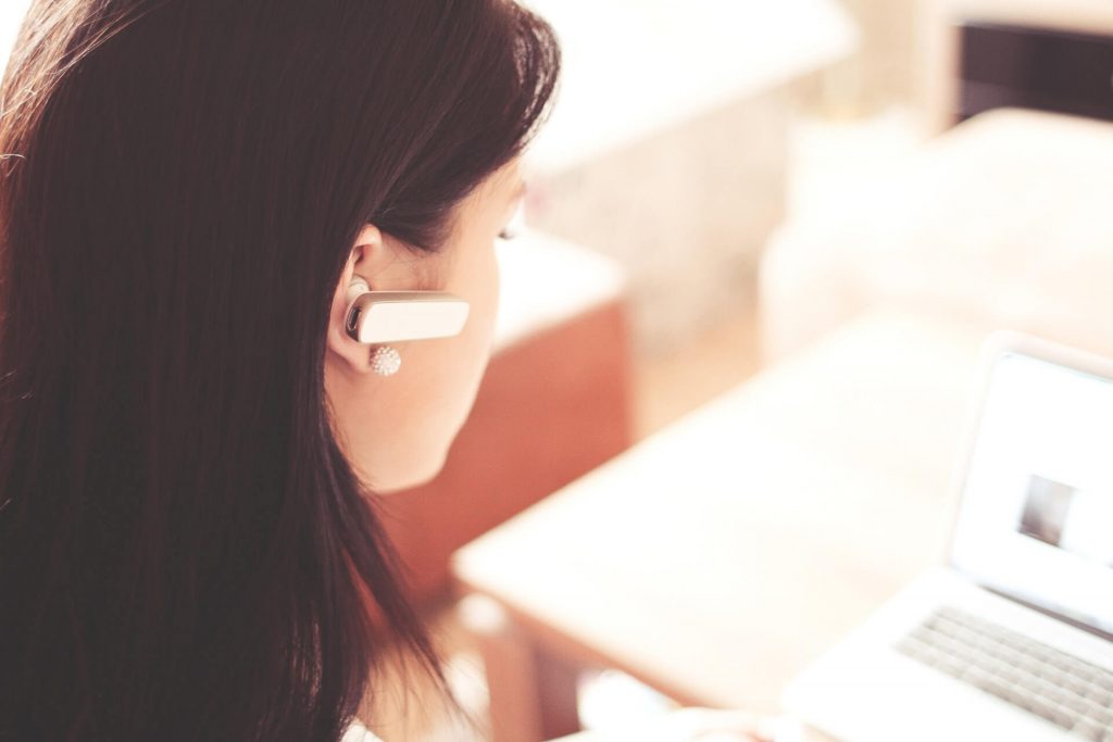 Woman working at computer while using a wireless earpiece.