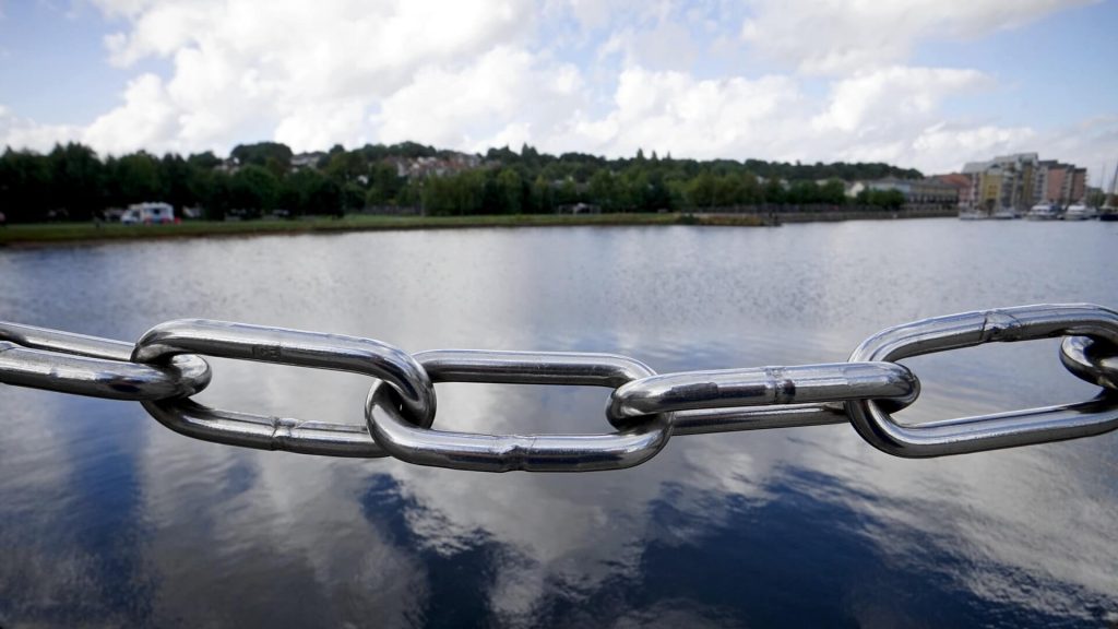 A chain of links stretched in front of a body of water.