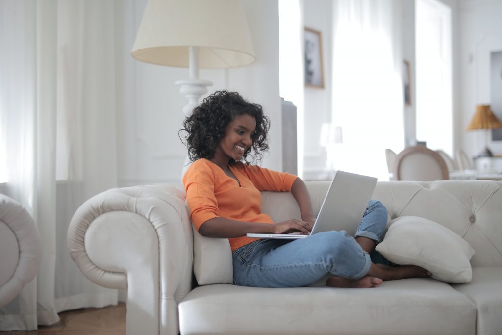 woman sitting on white couch using laptop computer