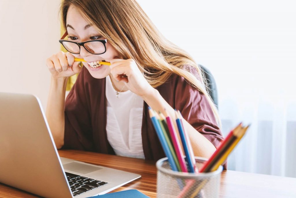 A woman looking at a laptop and chewing on a pencil.