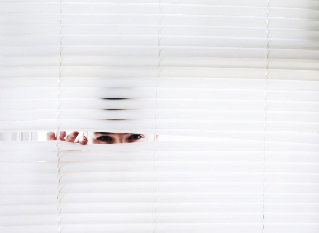 A man peeking through white blinds.