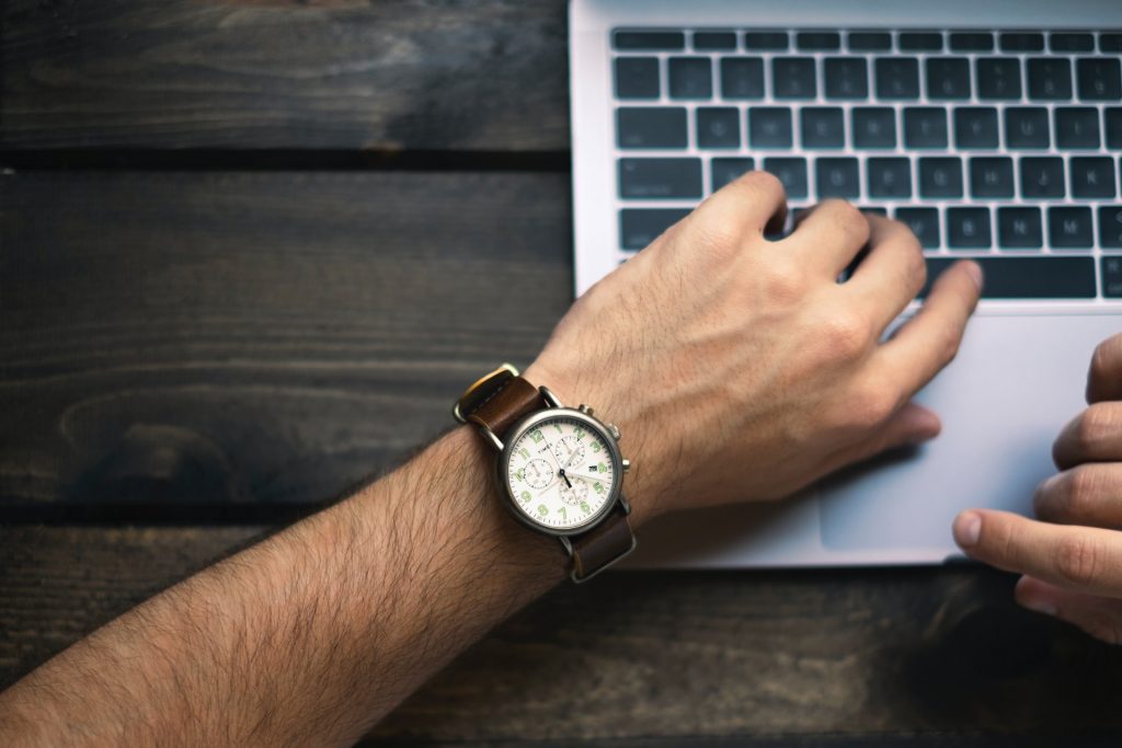 A hand with a watch resting on a laptop.