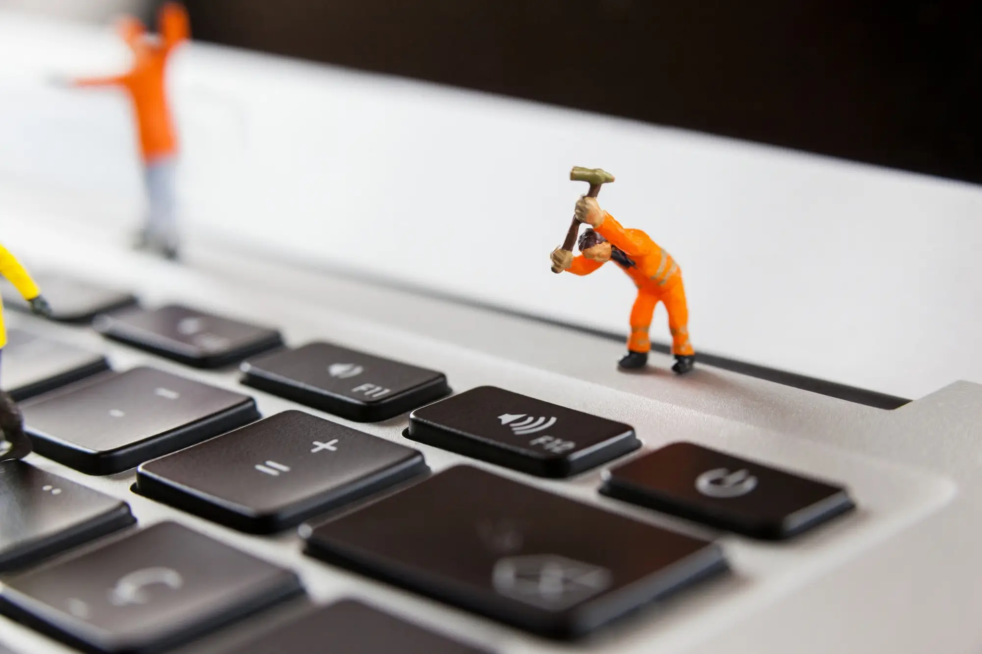 Miniature construction worker figurines working on a laptop keyboard.